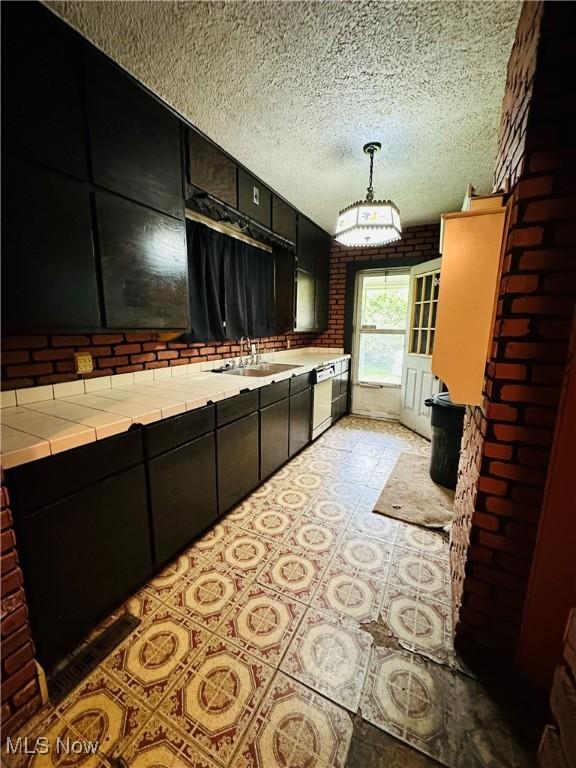 kitchen with dark cabinetry, a sink, tile countertops, dishwasher, and a textured ceiling