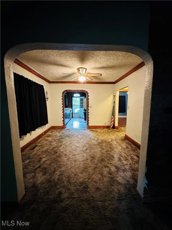 carpeted empty room with a textured ceiling, ornamental molding, baseboards, a ceiling fan, and arched walkways