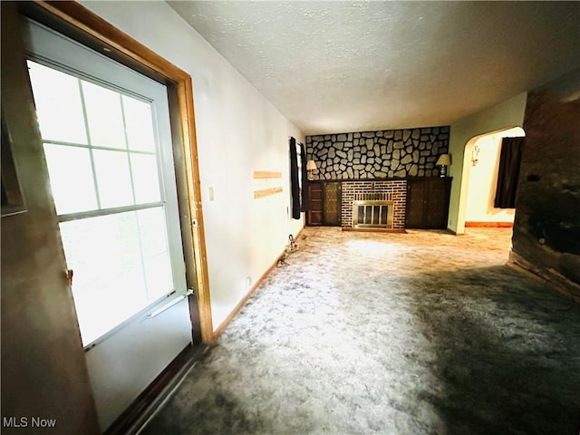 unfurnished living room featuring carpet, arched walkways, a fireplace, a textured ceiling, and baseboards