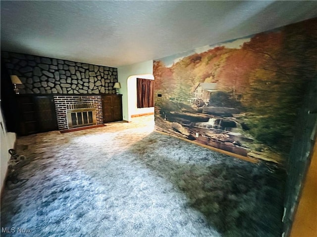 unfurnished living room with a glass covered fireplace, carpet floors, a textured ceiling, and arched walkways
