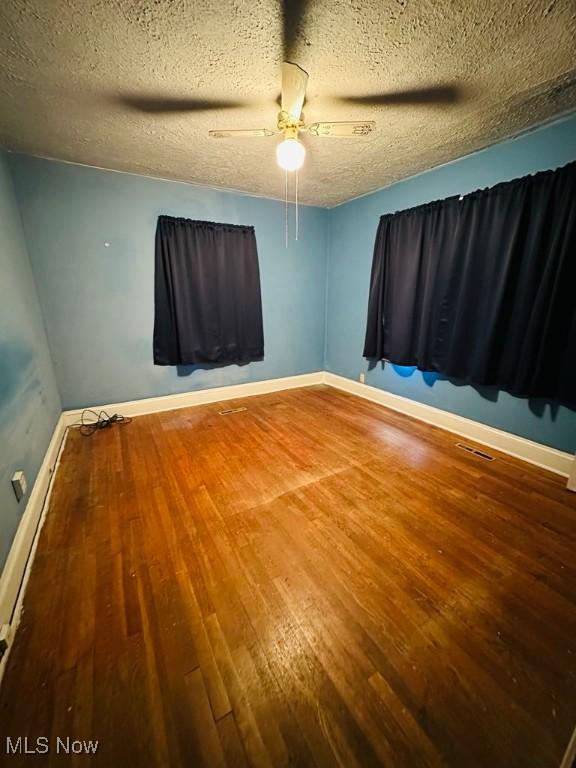 spare room with wood finished floors, ceiling fan, baseboards, and a textured ceiling