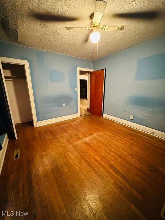 unfurnished bedroom featuring hardwood / wood-style flooring, baseboards, a closet, a textured ceiling, and ceiling fan