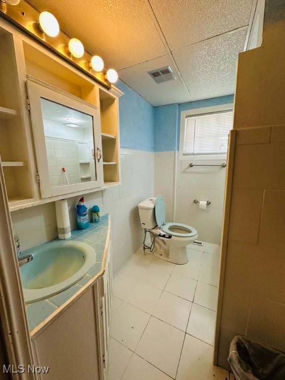 half bathroom featuring toilet, vanity, wainscoting, tile walls, and tile patterned flooring