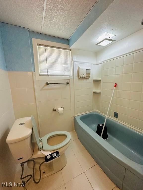 full bathroom with tile walls, toilet, tile patterned floors, a textured ceiling, and wainscoting