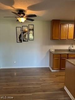kitchen with brown cabinetry, dark wood-style flooring, a ceiling fan, and baseboards