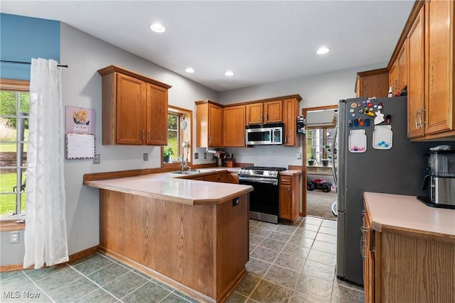 kitchen featuring appliances with stainless steel finishes, a peninsula, brown cabinets, recessed lighting, and light countertops