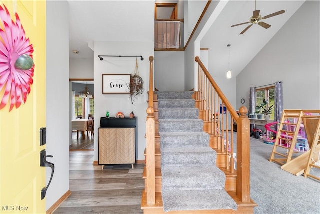 staircase with healthy amount of natural light, a ceiling fan, wood finished floors, and high vaulted ceiling