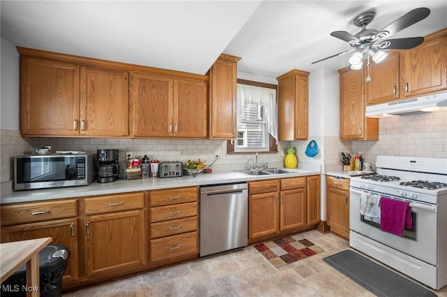 kitchen with appliances with stainless steel finishes, under cabinet range hood, a sink, and brown cabinets