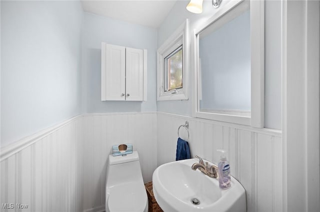 half bath featuring a sink, wainscoting, and toilet