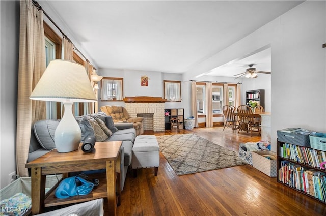living room with healthy amount of natural light, wood finished floors, ceiling fan, and a brick fireplace