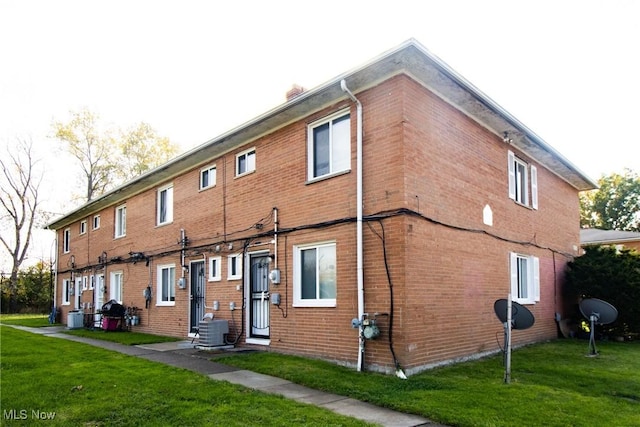 back of property with central AC unit, brick siding, and a lawn