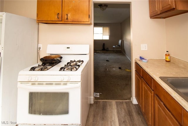 kitchen with white gas range, brown cabinetry, dark wood-type flooring, and a sink