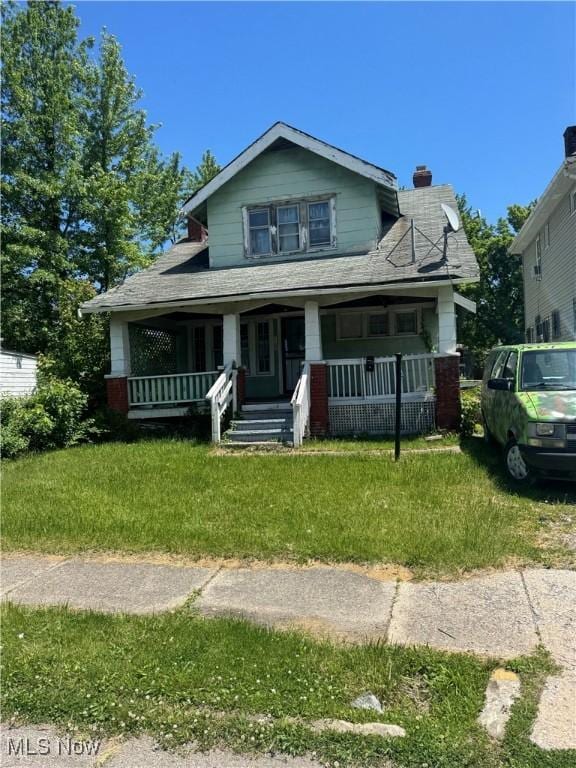 bungalow-style house featuring a porch, a front yard, and a chimney