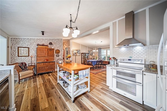 7214 Ridge Ave, Conneaut, OH 44030 - kitchen featuring range with two ovens, a chandelier, wall chimney range hood, light wood-style floors, and tasteful backsplash