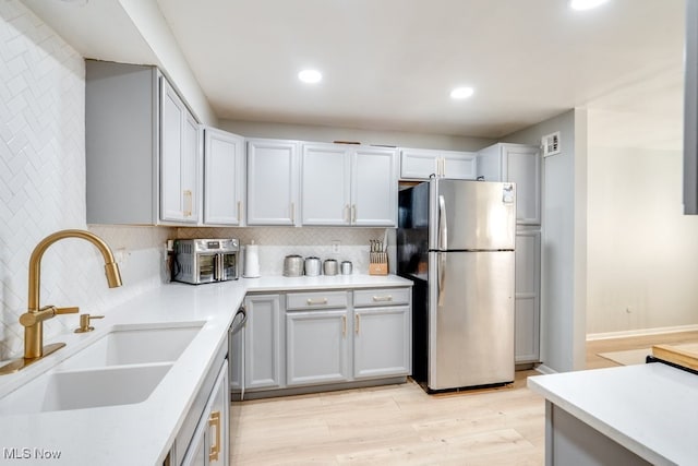 kitchen with appliances with stainless steel finishes, a sink, decorative backsplash, light countertops, and recessed lighting