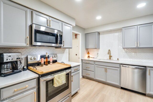 kitchen featuring stainless steel appliances, a sink, gray cabinets, tasteful backsplash, and light countertops