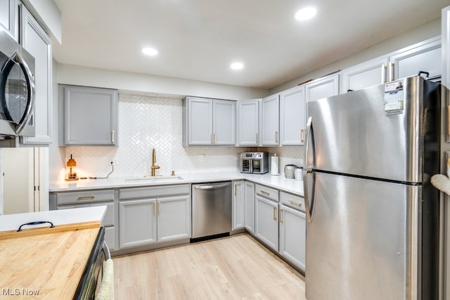 kitchen with stainless steel appliances, a sink, gray cabinetry, light wood-type flooring, and backsplash