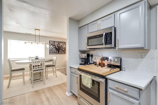 kitchen featuring stainless steel appliances, tasteful backsplash, light wood finished floors, light countertops, and gray cabinets