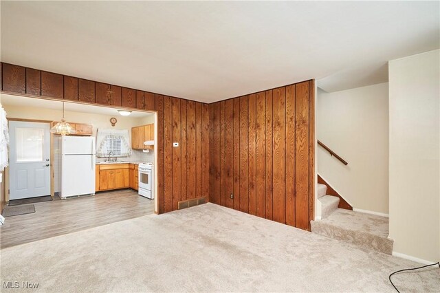 1658 Bronson Rd, Akron, OH 44305 - unfurnished living room featuring light carpet, a sink, stairs, wood walls, and baseboards
