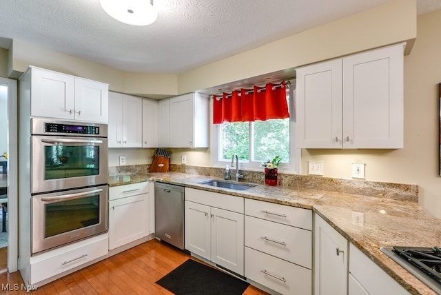 139 Elm Ct, Chagrin Falls, OH 44022 - kitchen with stainless steel appliances, a sink, light wood-type flooring, white cabinets, and a textured ceiling