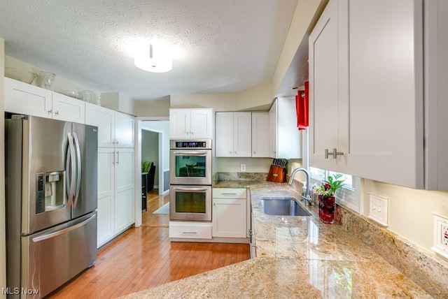 139 Elm Ct, Chagrin Falls, OH 44022 - kitchen featuring stainless steel appliances, a sink, white cabinets, light stone counters, and a textured ceiling