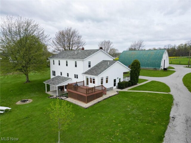 16321 Burton Windsor Rd, Middlefield, OH 44062 - rear view of house featuring an outdoor fire pit, a deck, a shingled roof, a lawn, and an outbuilding
