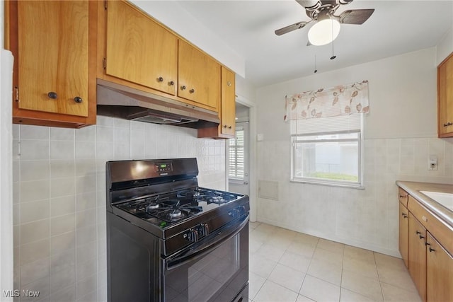 21031 Ball Ave, Euclid, OH 44123 - kitchen with black gas stove, under cabinet range hood, ceiling fan, light countertops, and light tile patterned floors