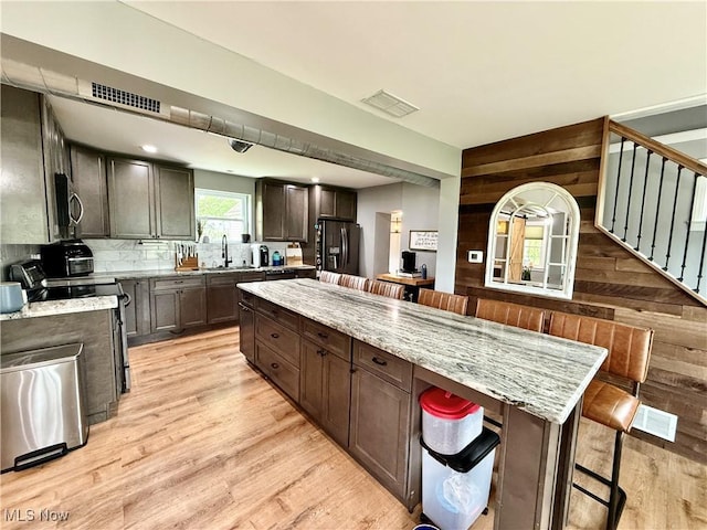 7509 S Palmyra Rd, Canfield, OH 44406 - kitchen featuring appliances with stainless steel finishes, wooden walls, light wood-style flooring, a sink, and a breakfast bar