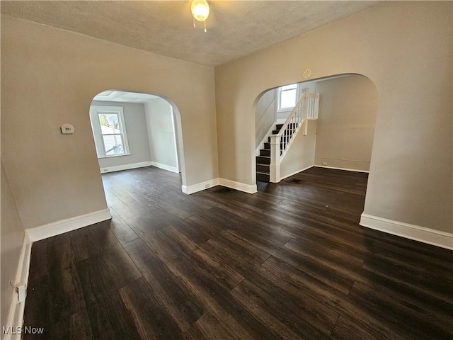 3891 W 21st St, Cleveland, OH 44109 - empty room featuring arched walkways, dark wood-style floors, baseboards, stairway, and a textured ceiling