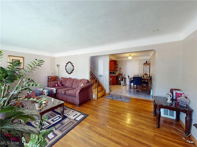 3882 Wallingford Rd, South Euclid, OH 44121 - living room featuring arched walkways, light wood-style flooring, a textured ceiling, and stairway