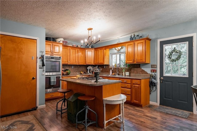 2993 Harris Hwy, Washington, WV 26181 - kitchen with stainless steel appliances, a chandelier, brown cabinets, a textured ceiling, and dark wood-style flooring