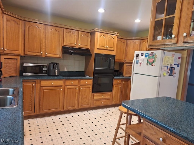 16604 Old State Rd, Middlefield, OH 44062 - kitchen with black appliances, under cabinet range hood, glass insert cabinets, brown cabinetry, and recessed lighting