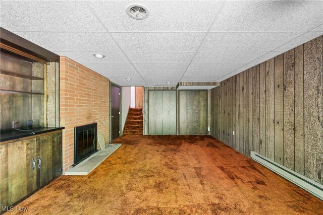 4512 Conestoga Trl, Copley, OH 44321 - unfurnished living room featuring a baseboard radiator, wooden walls, carpet flooring, a brick fireplace, and stairs