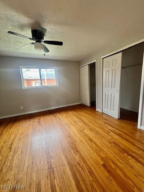 23855 Banbury Cir, Warrensville Heights, OH 44128 - unfurnished bedroom with wood finished floors, multiple closets, a textured ceiling, baseboards, and a ceiling fan