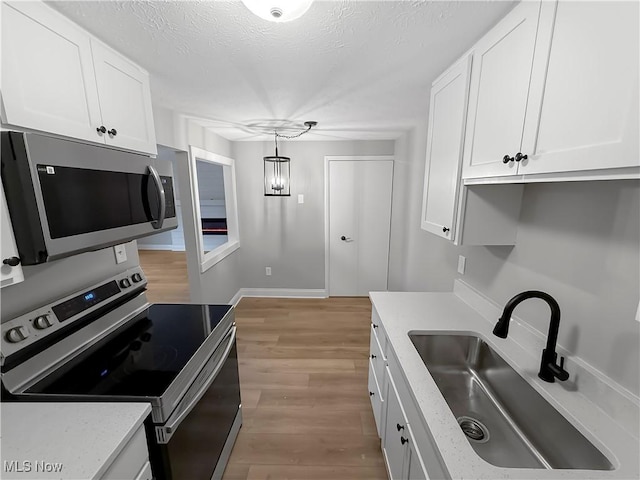 9530 Cove Dr Unit C-26, North Royalton, OH 44133 - kitchen with stainless steel appliances, a sink, white cabinets, light wood finished floors, and pendant lighting