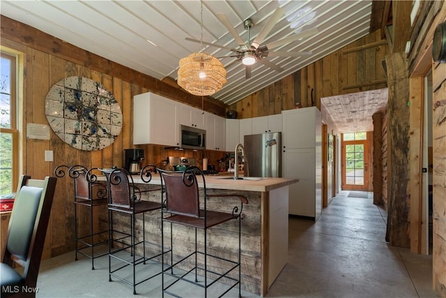 15216 Grove Rd SE, Port Washington, OH 43837 - kitchen featuring stainless steel appliances, wood walls, finished concrete floors, white cabinets, and a ceiling fan