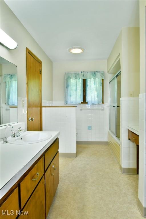 3763 E River Rd, Newton Falls, OH 44444 - bathroom with tile walls, a shower with shower door, vanity, a wainscoted wall, and a bathtub