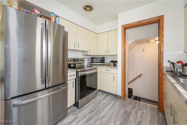 1923 15th St SW, Akron, OH 44314 - kitchen with stainless steel appliances, light wood-style flooring, cream cabinetry, and tasteful backsplash