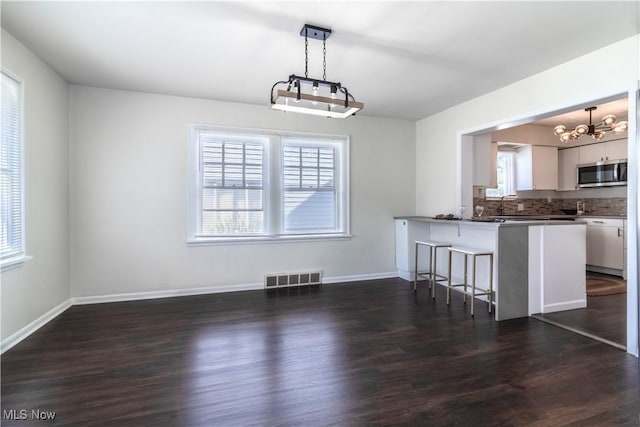 3525 Raymont Rd, University Heights, OH 44118 - kitchen with stainless steel microwave, a chandelier, white cabinetry, dark wood finished floors, and a kitchen breakfast bar
