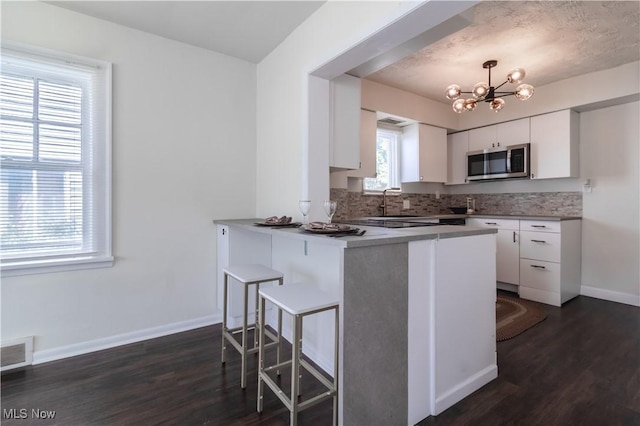 3525 Raymont Rd, University Heights, OH 44118 - kitchen with stainless steel microwave, white cabinetry, dark wood-style flooring, and a breakfast bar area