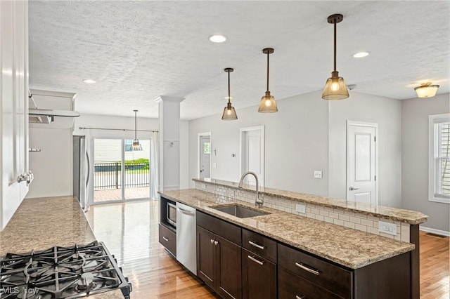 2450 Tremont Ave, Cleveland, OH 44113 - kitchen with stainless steel appliances, dark brown cabinets, an island with sink, a textured ceiling, and light wood-style floors