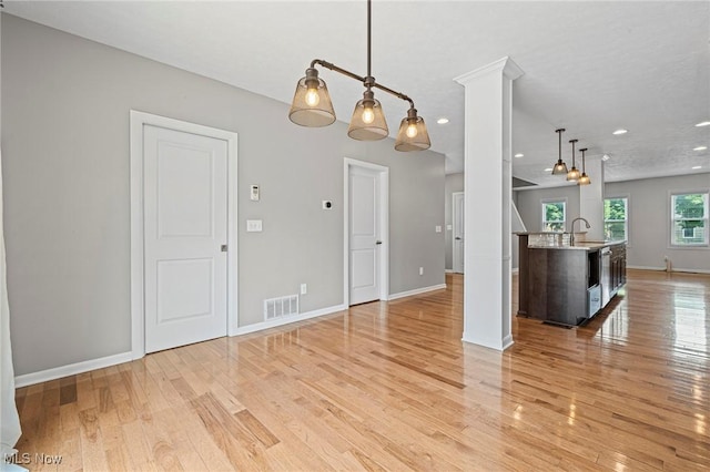 2450 Tremont Ave, Cleveland, OH 44113 - kitchen featuring light wood finished floors, hanging light fixtures, a kitchen island with sink, recessed lighting, and decorative columns