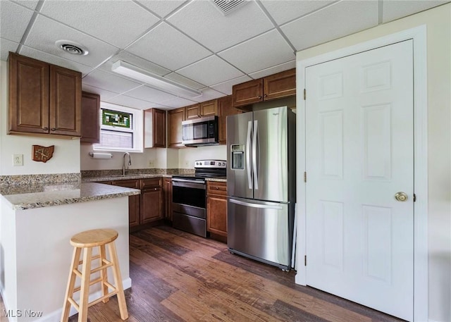 32094 Woodale Dr, Hanoverton, OH 44423 - kitchen featuring appliances with stainless steel finishes, a paneled ceiling, dark wood finished floors, a peninsula, and a kitchen bar