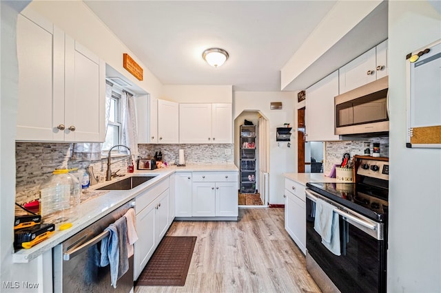 3906 Redfern Rd, Parma, OH 44134 - kitchen featuring stainless steel appliances, a sink, white cabinetry, decorative backsplash, and light wood-type flooring
