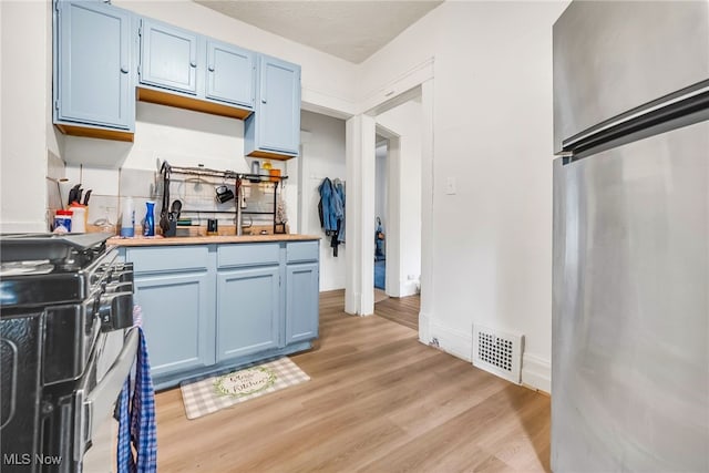 11020 Woodstock Ave, Cleveland, OH 44104 - kitchen with freestanding refrigerator, blue cabinets, range with gas stovetop, light wood-style floors, and tasteful backsplash