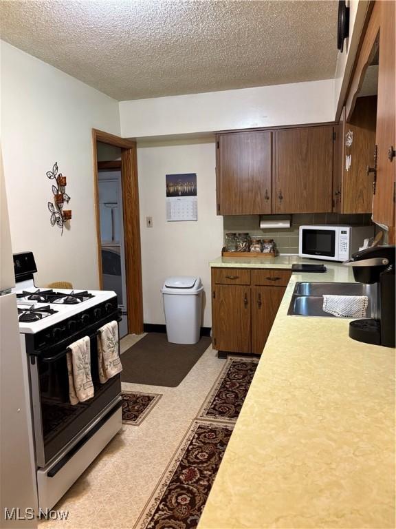 2499 Nesmith Lake Blvd, Akron, OH 44314 - kitchen featuring gas range oven, light countertops, white microwave, a textured ceiling, and a sink