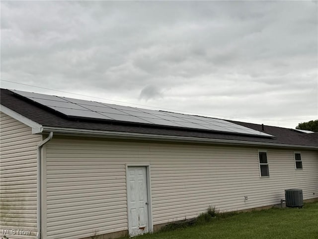 6920 Riverside Rd SE, Gnadenhutten, OH 44629 - view of property exterior with roof mounted solar panels, central air condition unit, roof with shingles, and a yard