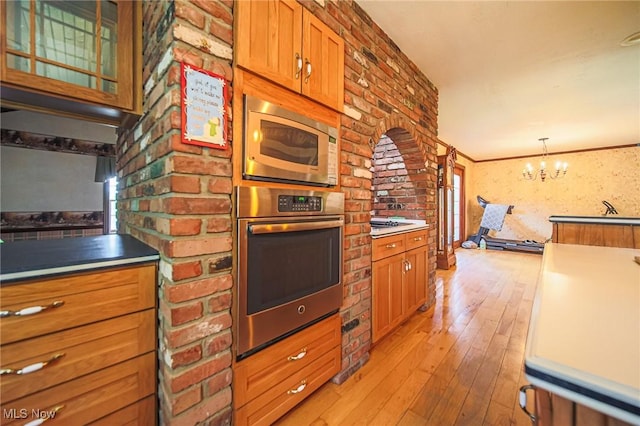 12793 New London Eastern Rd, Spencer, OH 44275 - kitchen with appliances with stainless steel finishes, light wood finished floors, brown cabinetry, a chandelier, and decorative light fixtures