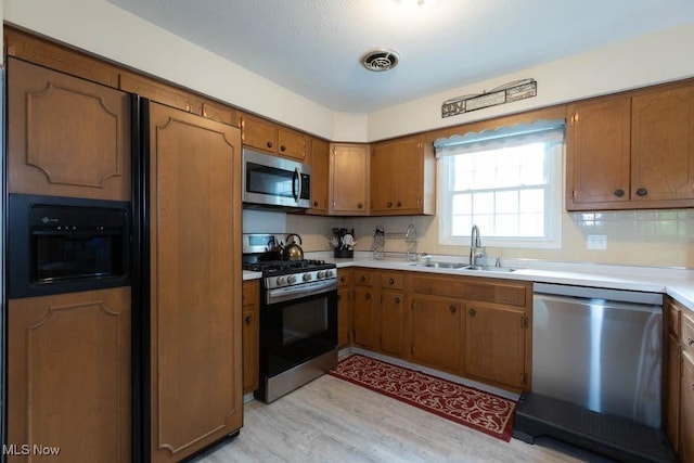 5940 Hansom Dr, Solon, OH 44139 - kitchen with appliances with stainless steel finishes, a sink, brown cabinetry, light wood finished floors, and light countertops