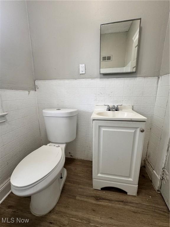 483 E 128th St, Cleveland, OH 44108 - half bath with tile walls, vanity, wood finished floors, toilet, and a wainscoted wall